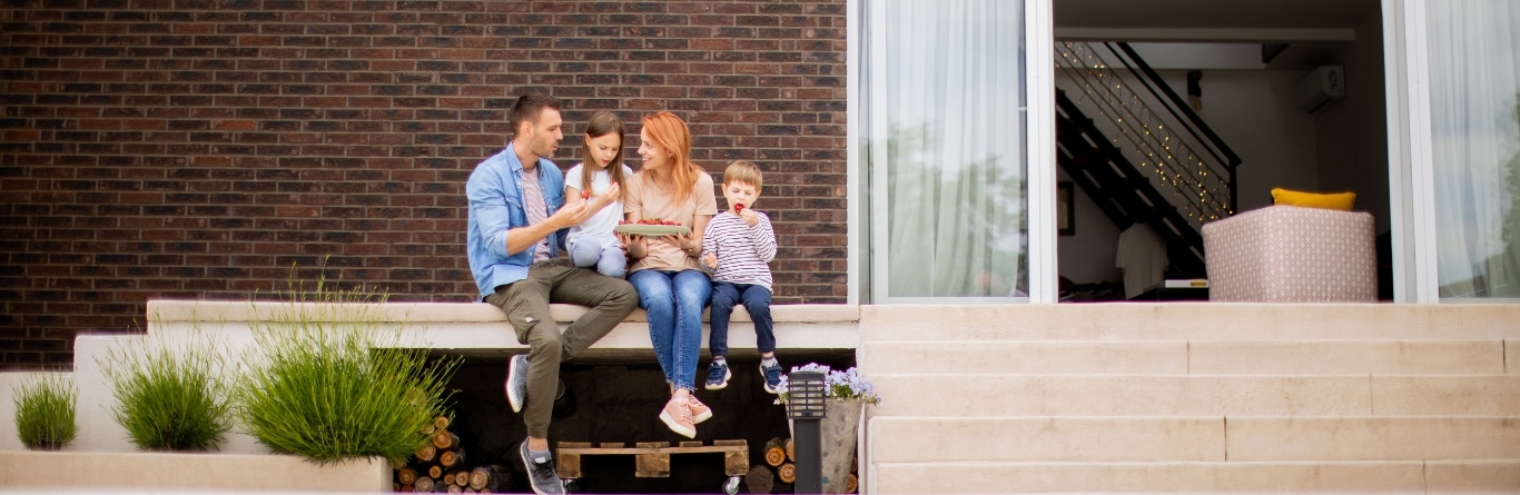 Familia feliz sentada en la entrada de su casa moderna disfrutando de una comida juntos